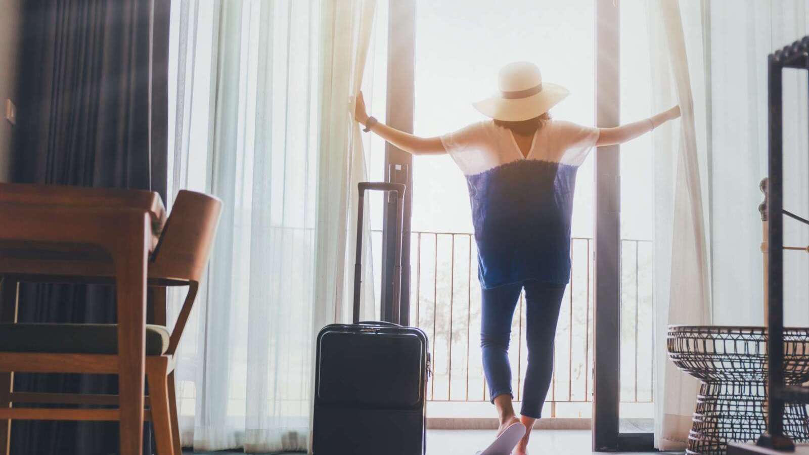 Asian women are staying in a hotel room with luggage.Open the curtain and  door in the room looking to outside view.Travel in holidays concept.Vintage tone.